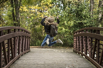 Woman jumping for joy on wooden bridge in autumn forest