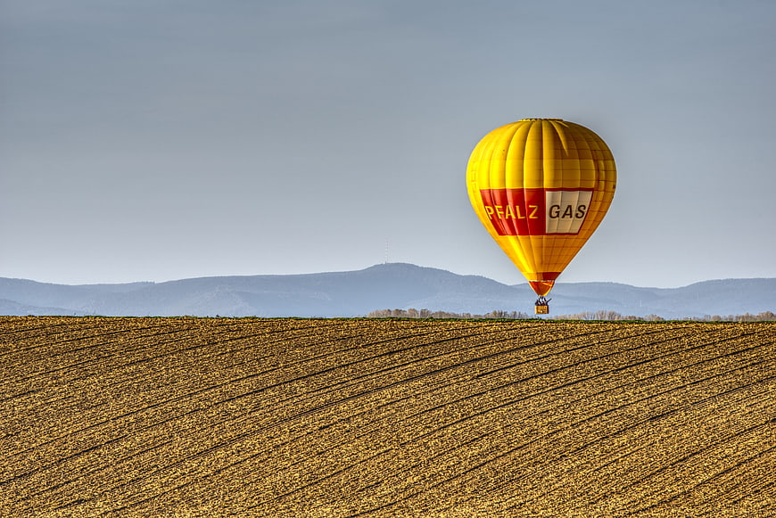 Yellow hot air balloon flying over plowed field