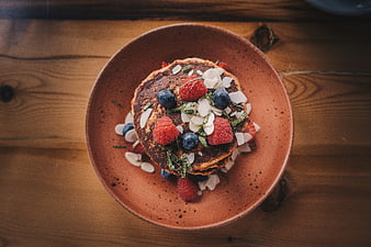 Overhead shot of pancakes with berries and coconut flakes on wooden table