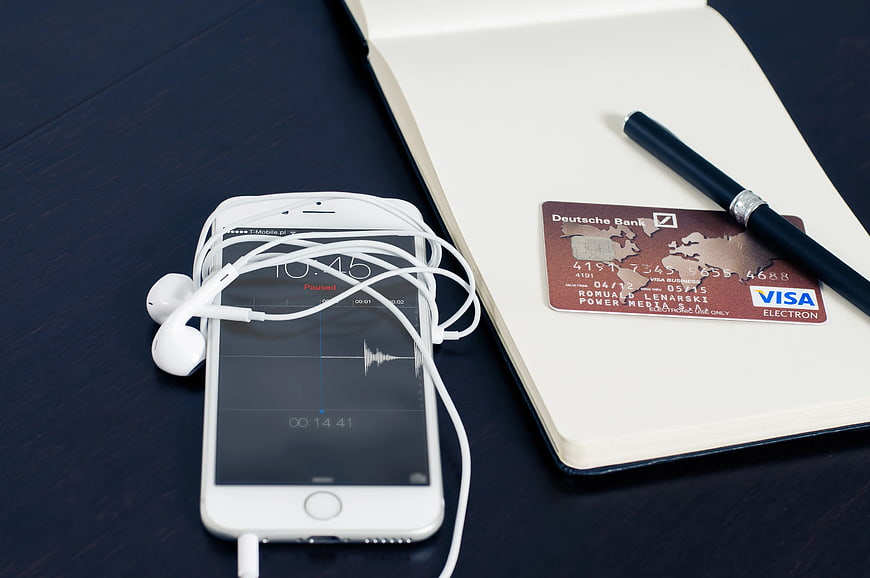 White smartphone with headphones, notebook, and credit card on dark desk