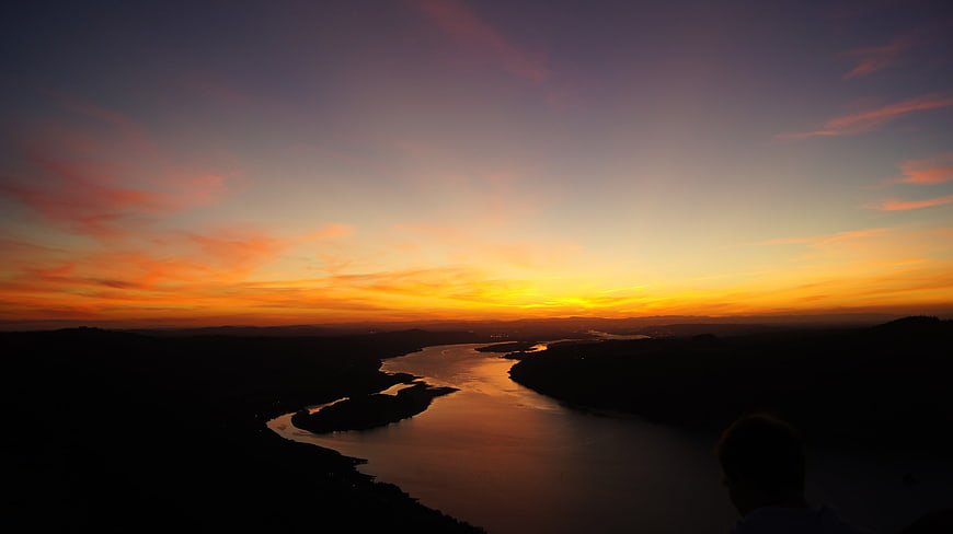 Silhouette of person watching vibrant sunset over winding river