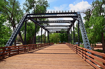 Wooden pedestrian bridge with metal truss in green park