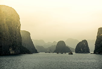Misty limestone karsts and boats in Ha Long Bay at sunrise