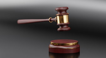 Wooden judge gavel with gold accents hovering above sound block on dark background