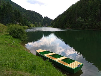 Green wooden boat on calm river in forest valley