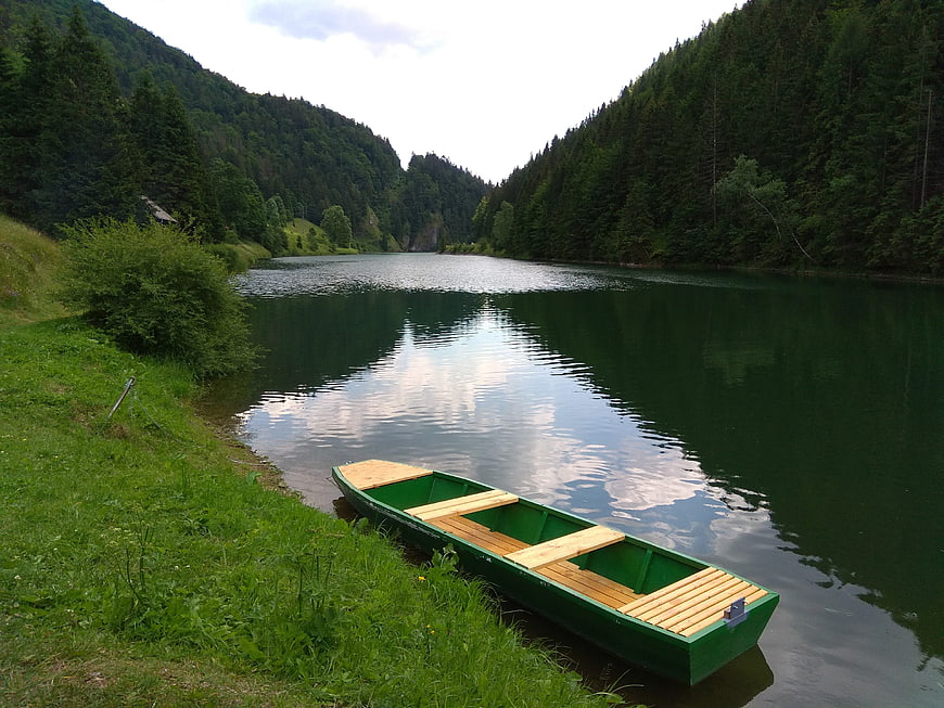 Green wooden boat on calm river in forest valley