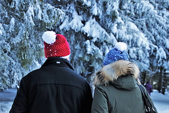 Couple in winter hats walking through snowy forest