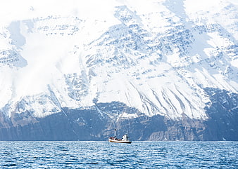 Small boat sailing in front of massive snow-covered mountains