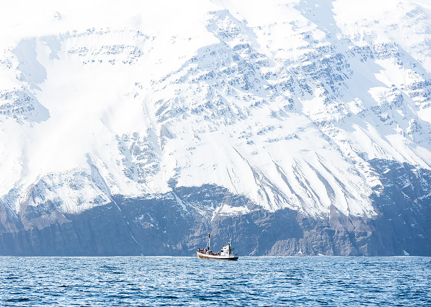 Small boat sailing in front of massive snow-covered mountains