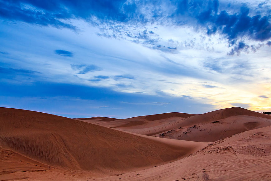 Vast Sand Dunes Under Dramatic Blue Sky at Sunset