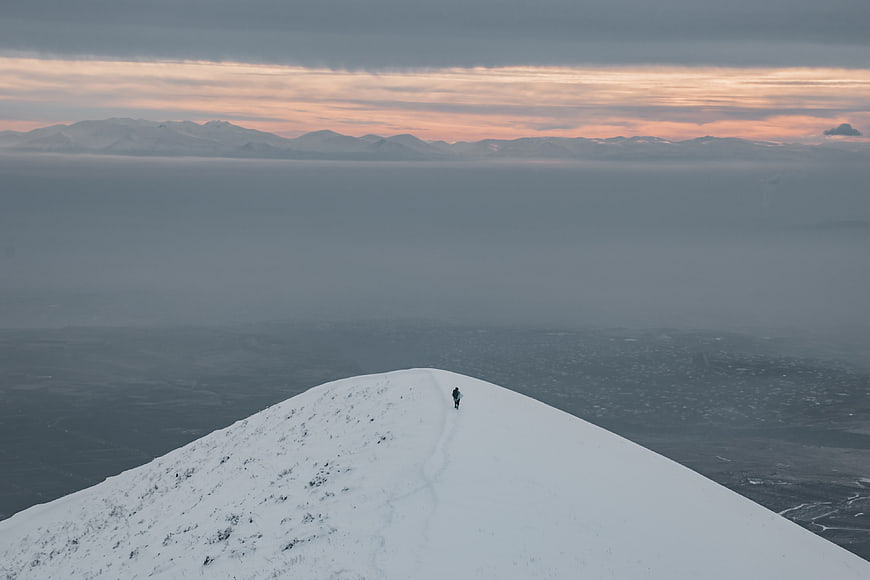 Lone Hiker on Snowy Mountain Ridge at Sunset