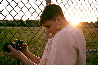 Young Photographer Reviewing Camera by Chain Link Fence at Sunset