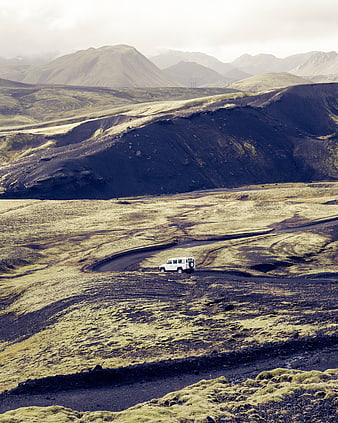 White SUV driving on winding road through mossy volcanic highlands