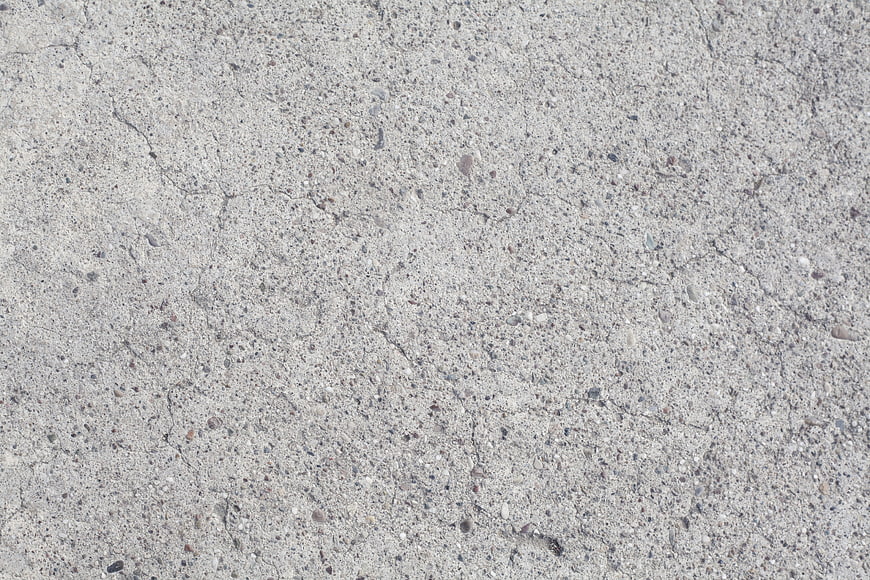 Close-up of rough gray concrete surface texture with cracks and aggregate