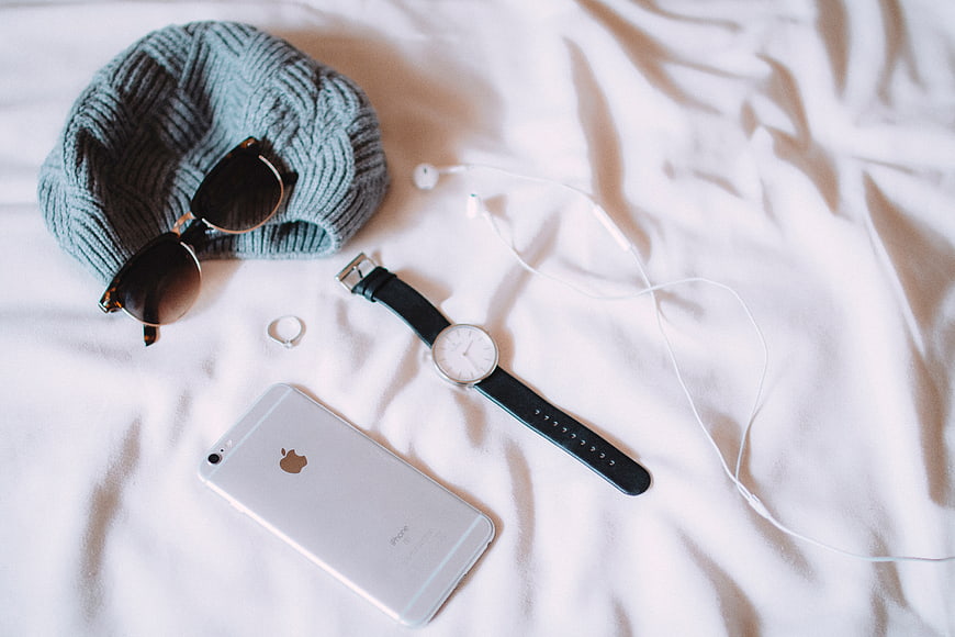 Flat lay of fashion accessories and smartphone on white bed sheets
