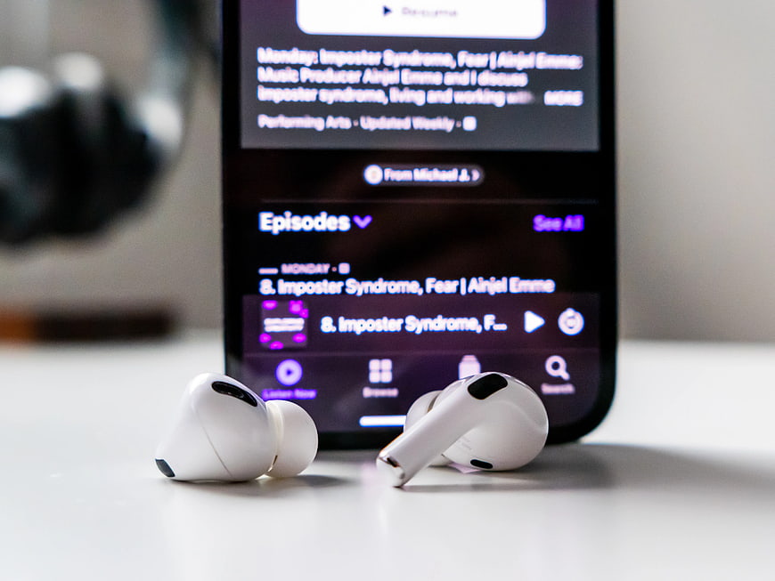 White wireless earbuds and smartphone displaying podcast app