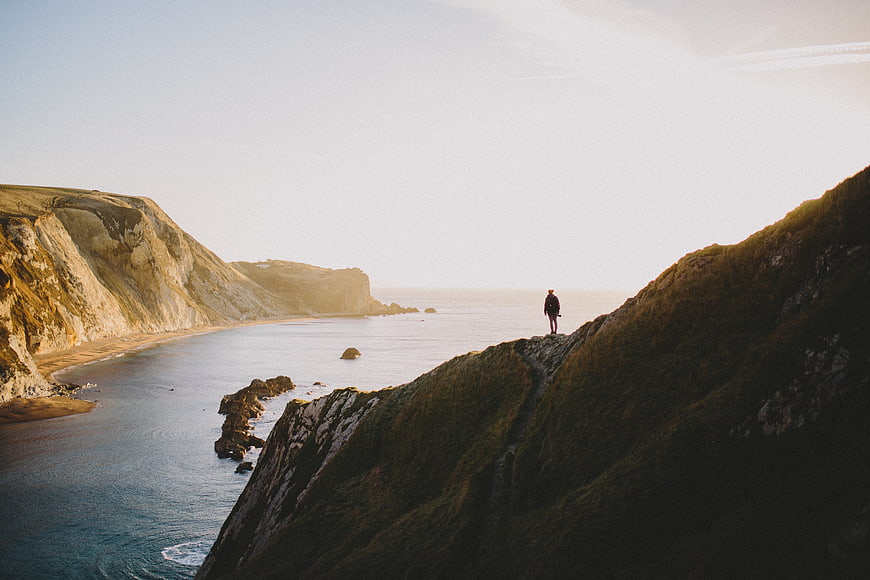 Lone Hiker on Coastal Cliff Overlooking Ocean at Sunset