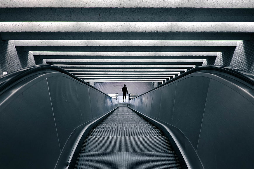 Silhouette of Man Walking Up Escalator in Modern Subway Station