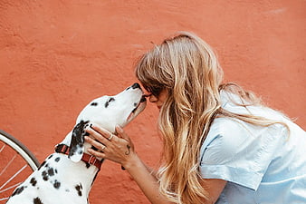 Blonde Woman Kissing Dalmatian Dog Against Orange Wall