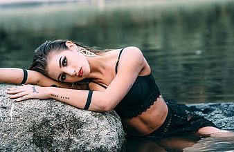 Young woman in black lingerie posing on a rock by a lake
