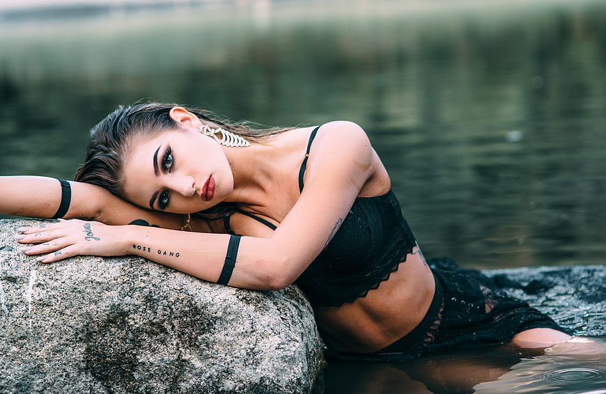 Young woman in black lingerie posing on a rock by a lake