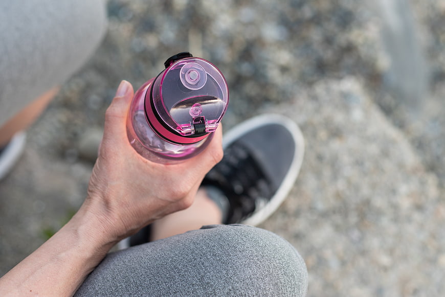 Hand holding pink water bottle during outdoor fitness break
