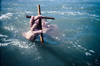 Hand holding wooden cross emerging from blue ocean water
