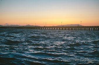 Sunset over choppy ocean with long pier silhouette