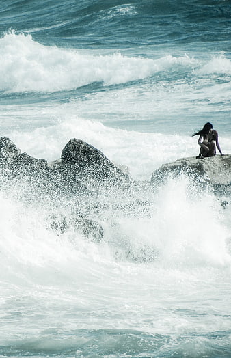 Woman sitting on rock amidst crashing ocean waves