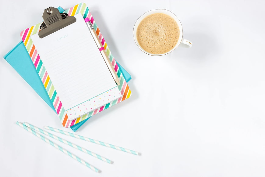 Flat lay of colorful clipboard, coffee cup, and stationery on white background