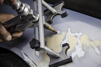 Close-up of mechanic using dent puller tool on car body panel