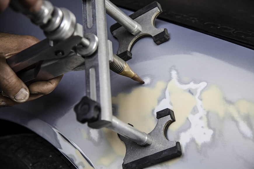 Close-up of mechanic using dent puller tool on car body panel