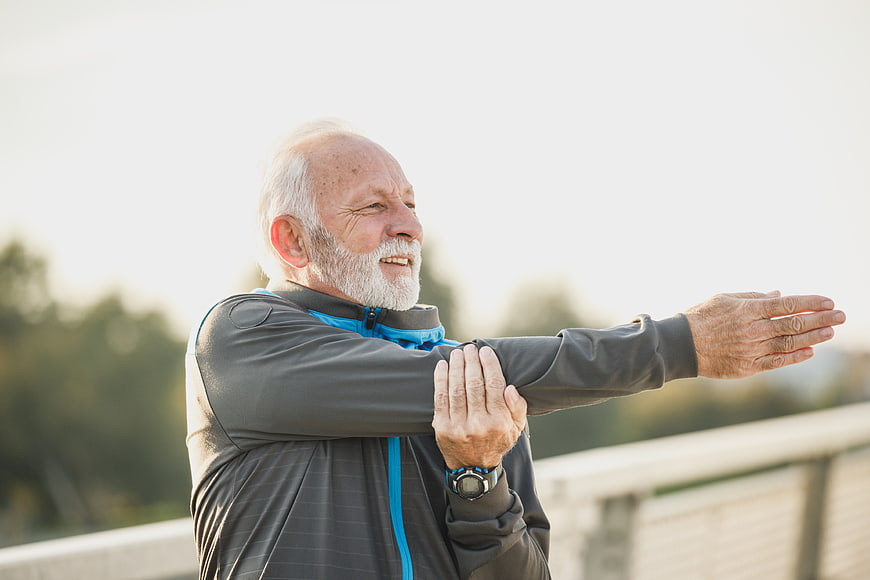 Senior man stretching arm outdoors after morning run