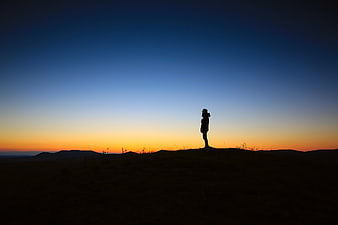 Silhouette of woman standing on hill at sunset