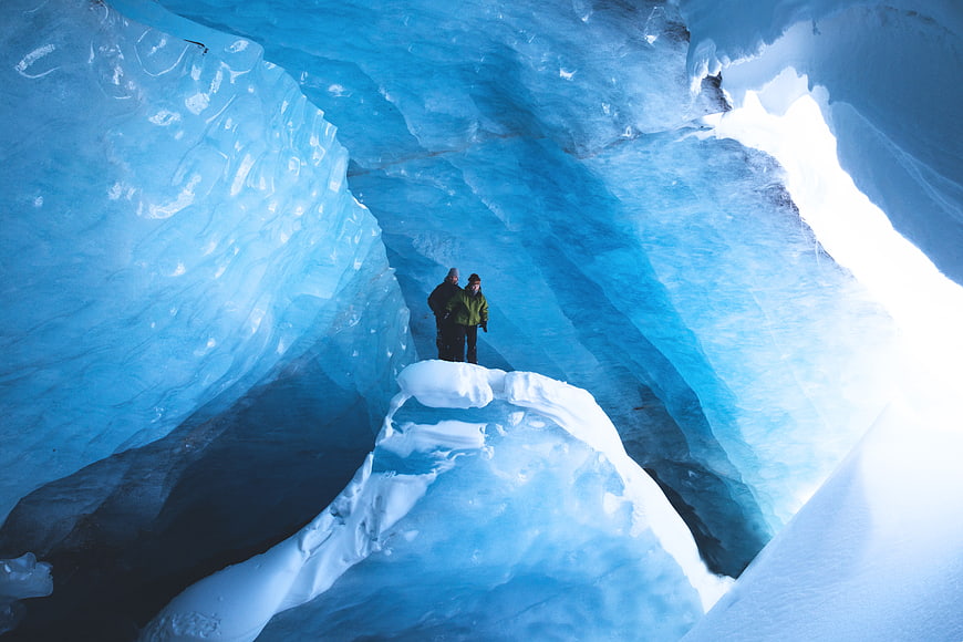Two explorers standing inside a vibrant blue ice cave