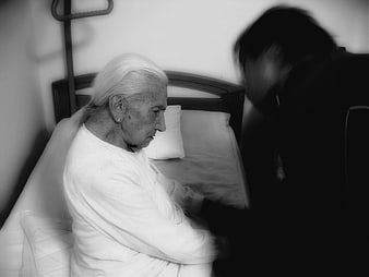 Black and white photo of elderly woman in bed with blurred caregiver