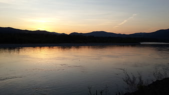 Serene River Sunset with Mountain Silhouettes and Golden Reflections