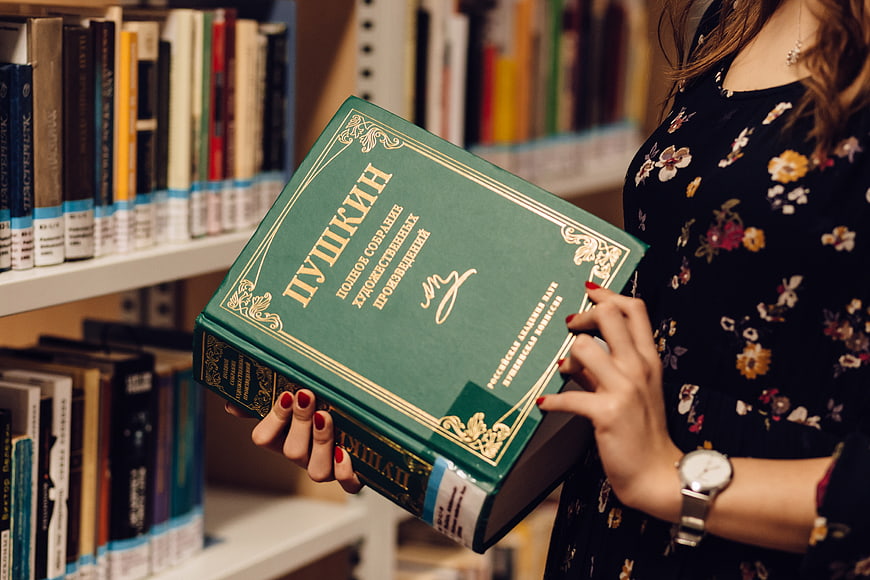 Woman holding green Pushkin book in library