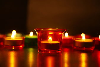 Glowing Red Diya Oil Lamp With Surrounding Candles On Dark Surface