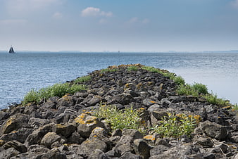 Rocky Jetty Leading to Blue Sea with Distant Sailboat