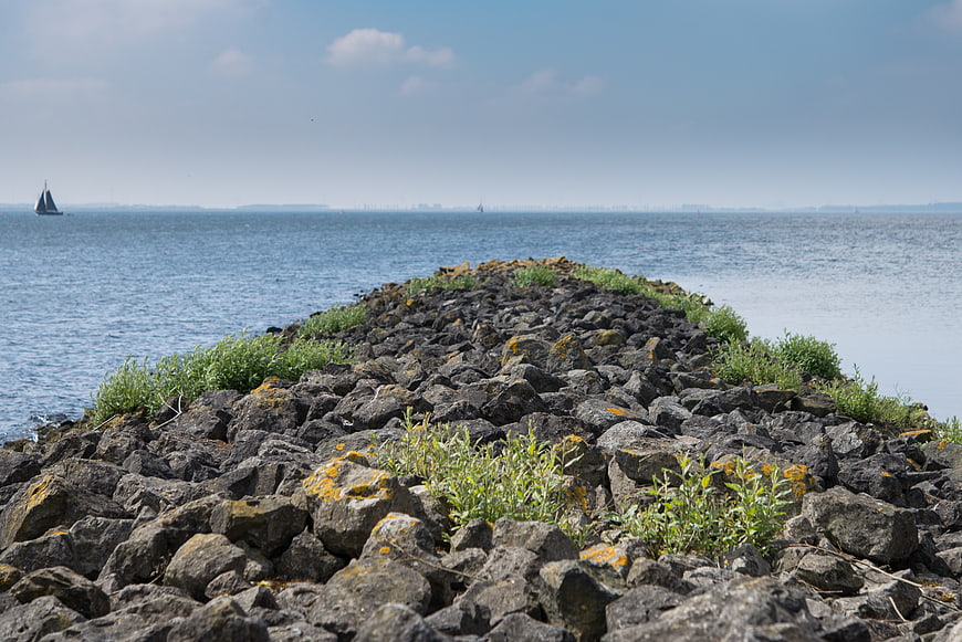 Rocky Jetty Leading to Blue Sea with Distant Sailboat