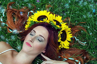 Redhead woman with sunflower crown lying in grass