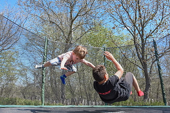 Two children jumping and playing on an outdoor trampoline