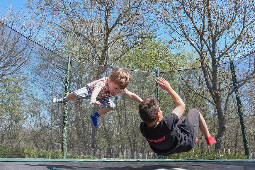 Two children jumping and playing on an outdoor trampoline