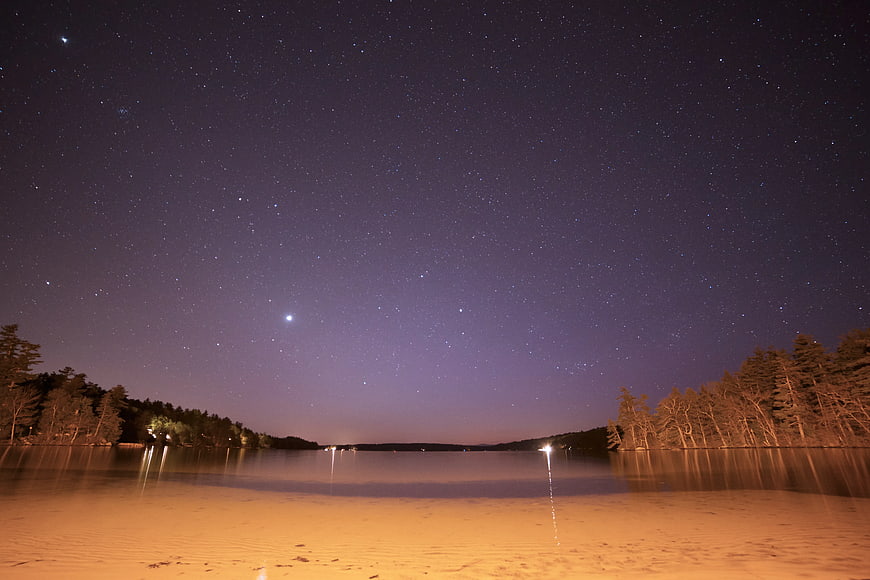 Starry Night Sky Over Lake With Sandy Beach