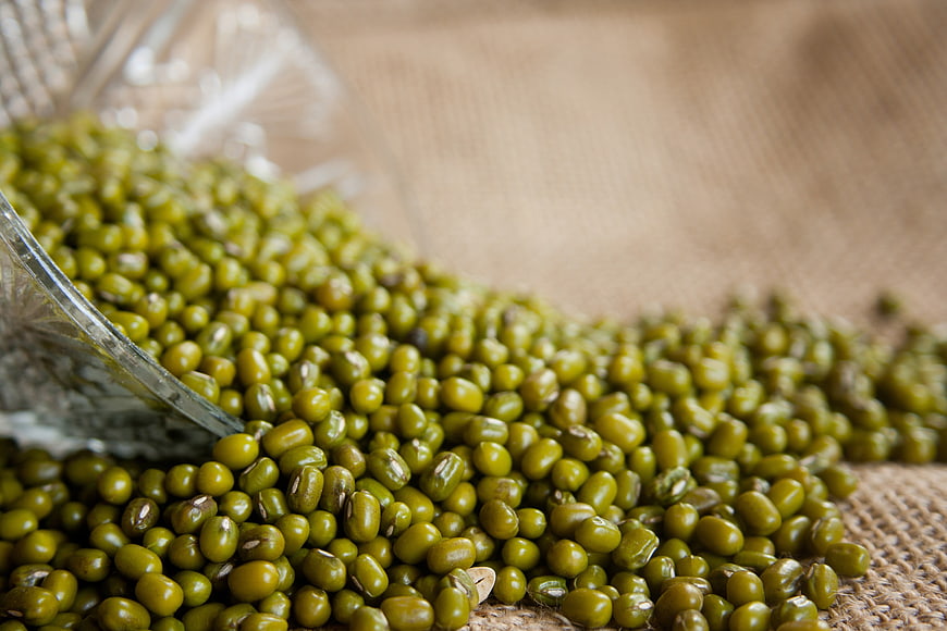 Close-up of raw green mung beans spilling from a glass bowl onto burlap