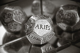 Black and white close-up of a metal dodecahedron die showing Aries