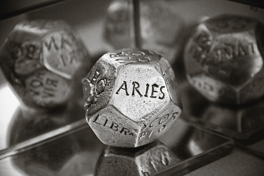 Black and white close-up of a metal dodecahedron die showing Aries
