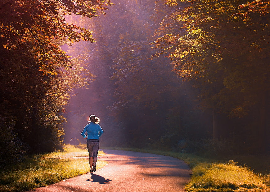 Woman jogging on a misty forest path at sunrise