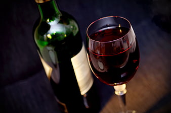 Red wine glass and bottle on dark wooden table
